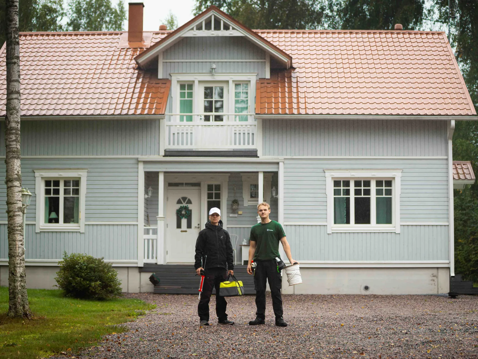 TiivisKodin asentajat vaalean puutalon pihassa työvälineineen